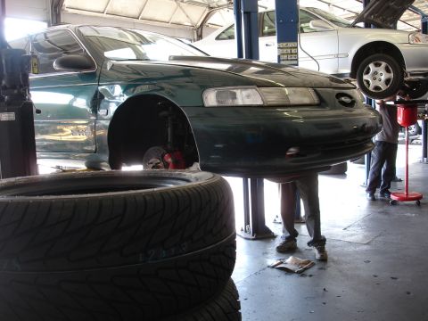 1993 Ford Taurus - A green 1993 Ford Taurus is shown on a lift in a service bay, with new tires stacked in front.