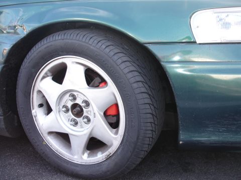 1993 Ford Taurus - Close-up of a green 1993 Ford Taurus's front wheel and fender, highlighting the tire and red brake caliper.