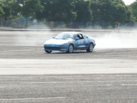 2001 Mercury Grand Marquis - Blue sports car with racing numbers drifts on a track, kicking up tire smoke.