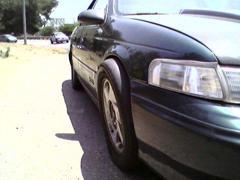 1993 Ford Taurus - A dark 1993 Ford Taurus is seen from the front quarter, with a clear view of its headlight and wheel.