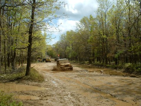 1991 Ford Bronco - Off-road vehicles tackle a challenging muddy trail in a forest setting.