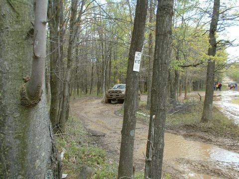 1991 Ford Bronco - Multiple SUVs navigate a challenging muddy trail through a wooded area.