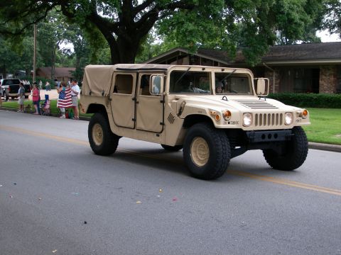 2000 Ford Crown Victoria - A tan Humvee with a canvas top drives down a street, observed by onlookers holding an American flag.