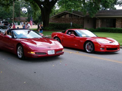 2000 Ford Crown Victoria - Two red Corvettes participate in a parade, with spectators and flags lining the street.