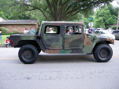 2000 Ford Crown Victoria - A military-style Humvee participates in a parade, observed by onlookers on the side of the road.