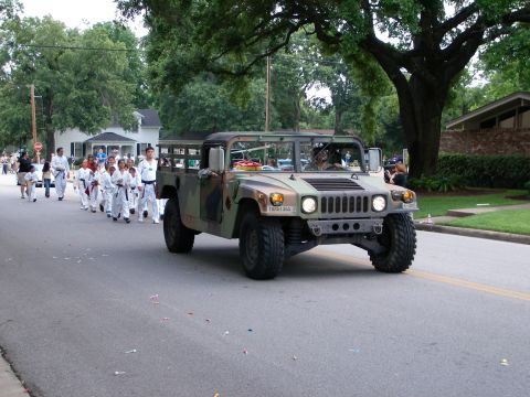 2000 Ford Crown Victoria - Humvee leads a parade group of martial artists on a tree-lined street.