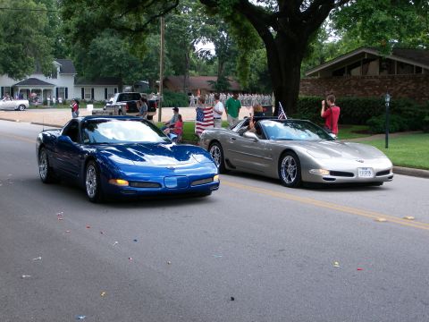 2000 Ford Crown Victoria - Two Chevrolet Corvettes, a blue coupe and a silver convertible, participate in a parade with spectators lining the street.