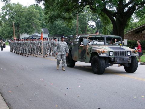 2000 Ford Crown Victoria - A military Humvee drives alongside soldiers marching in formation during a parade.