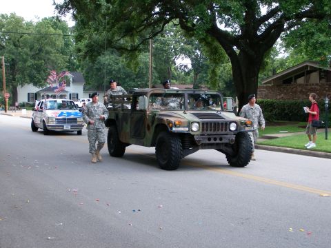 2000 Ford Crown Victoria - Military vehicles participate in a parade, with soldiers marching alongside a Humvee and a decorated car.