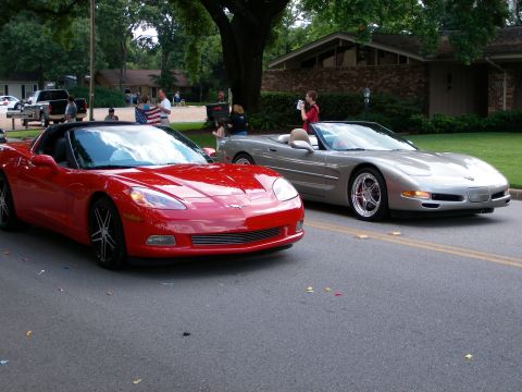 2000 Ford Crown Victoria - Two Chevrolet Corvettes, a red one and a silver one, are parked on a street during what appears to be a parade.
