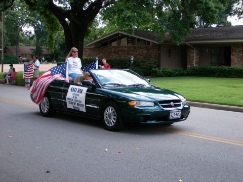 2000 Ford Crown Victoria - A green convertible sedan participates in a parade, adorned with American flags and banners.