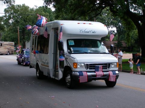 2000 Ford Crown Victoria - A white RV, decorated with American flags and balloons, participates in a parade.