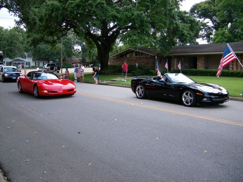 2000 Ford Crown Victoria - Two convertibles, a red and a black Corvette, participate in a parade with spectators and flags.