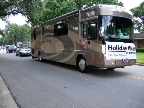 2000 Ford Crown Victoria - An RV participates in a parade, displaying a banner for 'Holiday World of Houston' and followed by a convertible and a sedan.