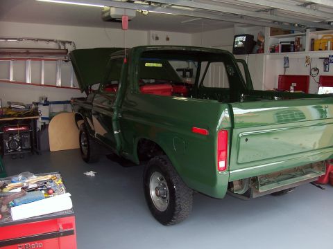 1978 Ford Bronco - A green pickup truck is parked inside a garage with its hood and tailgate open, revealing its red interior.