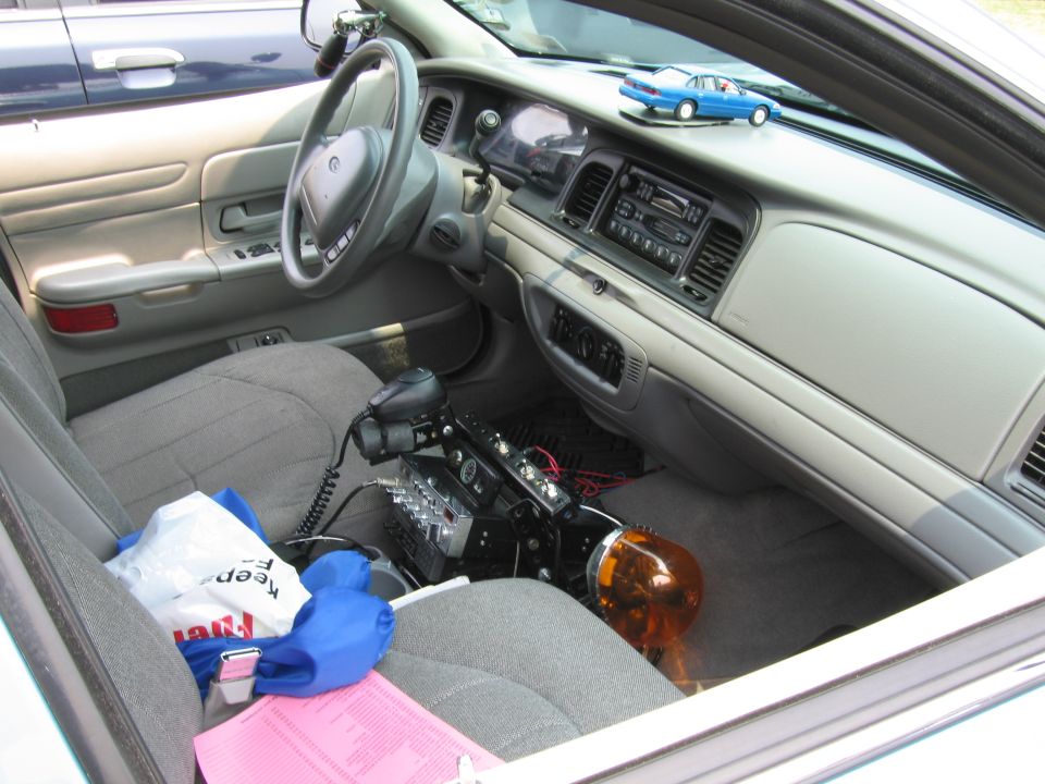 Interior of a police car, showing the steering wheel, dashboard, and center console with radio equipment and an orange light