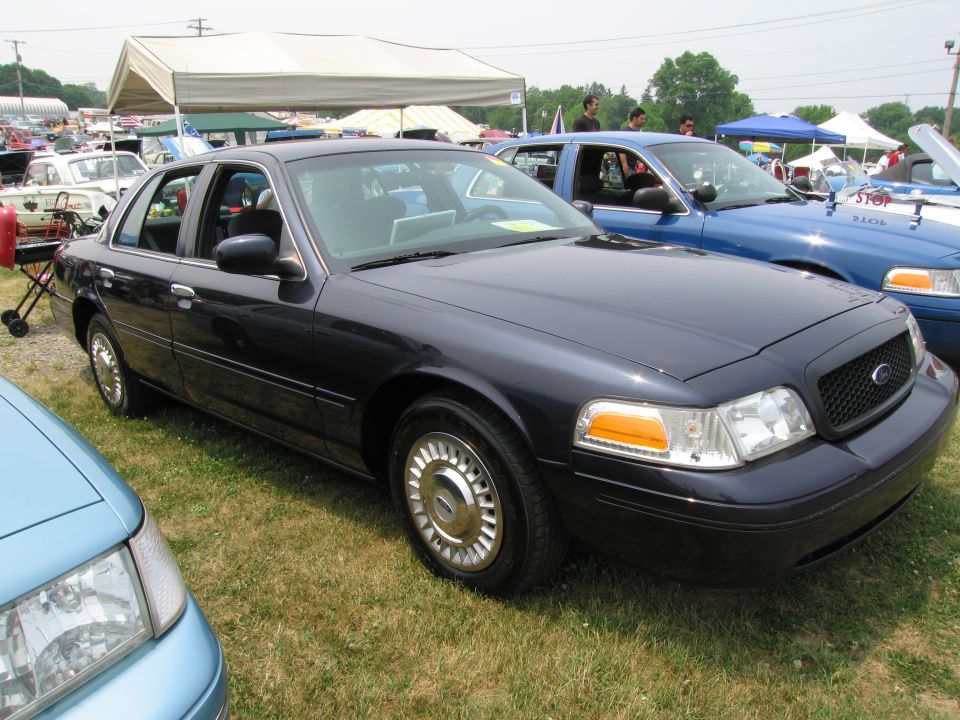 Dark blue Ford Crown Victoria parked on grass, another blue Crown Victoria behind it