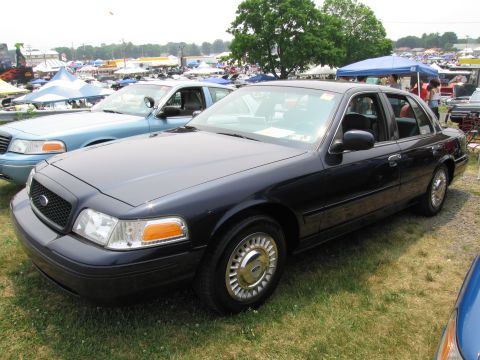 1991 Ford LTD Crown Victoria - Two Ford Crown Victorias are parked on a grassy field at an outdoor event with tents in the background.