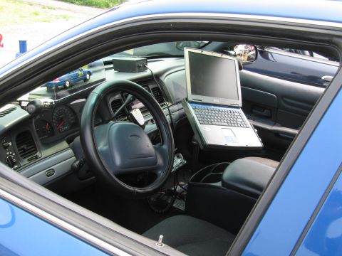 1991 Ford LTD Crown Victoria - The interior of a blue police car is shown, a laptop mounted on the passenger side and a miniature police car on the dashboard.