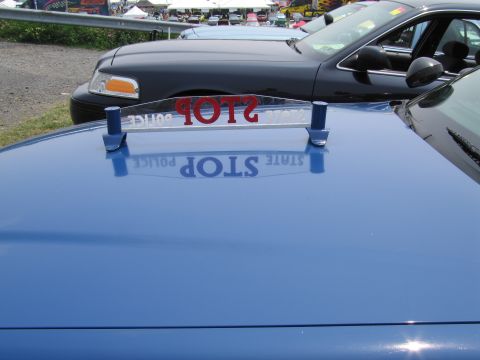1991 Ford LTD Crown Victoria - Reflection of a "STOP POLICE STATE" sign on the hood of a blue police car, with another police car behind it.