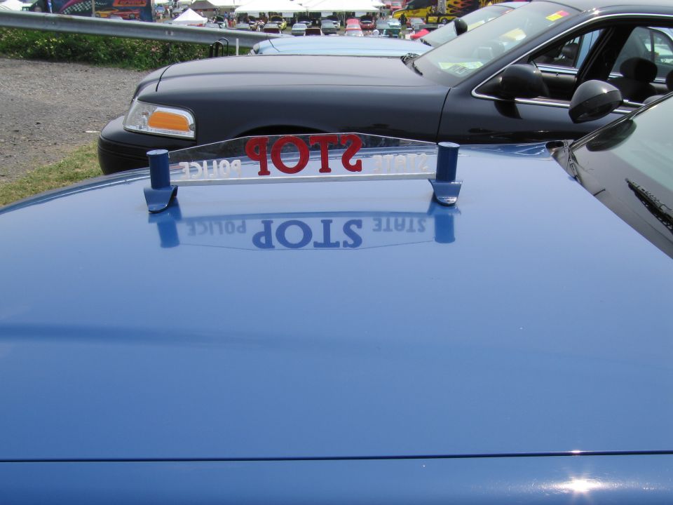 Blue police car hood with reflection of "STOP POLICE STATE" sign. Black police car in background