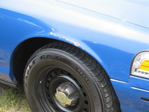 1991 Ford LTD Crown Victoria - Close-up of a blue sedan's front fender and wheel, showing some rust near the wheel well.