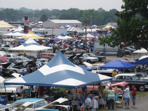 1991 Ford LTD Crown Victoria - A busy outdoor car show features many vehicles and tents, with people milling around.