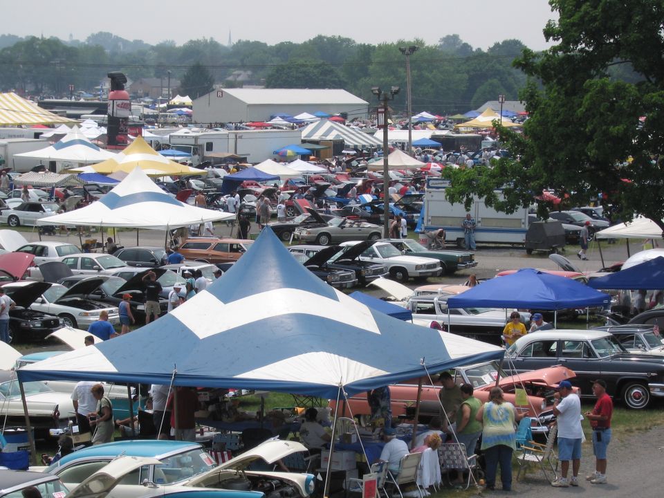 Outdoor car show with numerous tents and vehicles parked and displayed under them