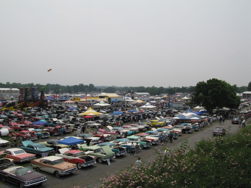 Wide view of a car show with rows of classic cars and tents under a hazy sky