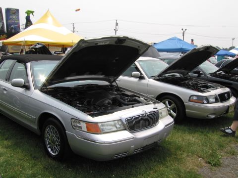 1991 Ford LTD Crown Victoria - Two sedans with their hoods open at an outdoor event. The front vehicle appears to be a Mercury Grand Marquis.