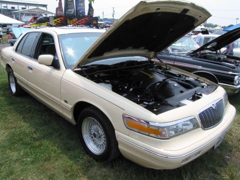 1991 Ford LTD Crown Victoria - A cream-colored Mercury Grand Marquis is displayed with its hood open at an outdoor event.