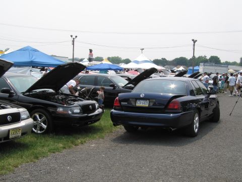 1991 Ford LTD Crown Victoria - A dark blue sedan is parked with its trunk open at an outdoor car show, with other vehicles and tents visible in the background.