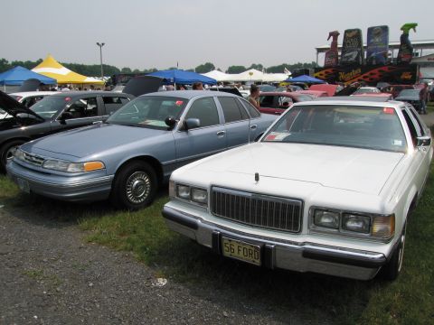 1991 Ford LTD Crown Victoria - A light blue 1991 Ford Crown Victoria is parked at an outdoor event next to a white sedan, with tents and displays in the background.