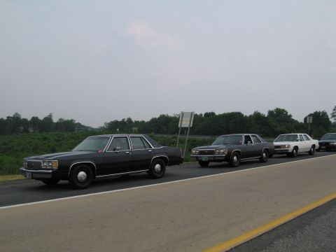1991 Ford LTD Crown Victoria - Four Ford Crown Victorias drive in formation on a highway under an overcast sky.