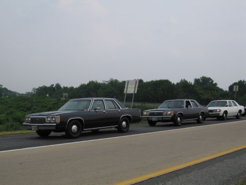 1991 Ford LTD Crown Victoria - A trio of Ford Crown Victorias are traveling down the road on a cloudy day.