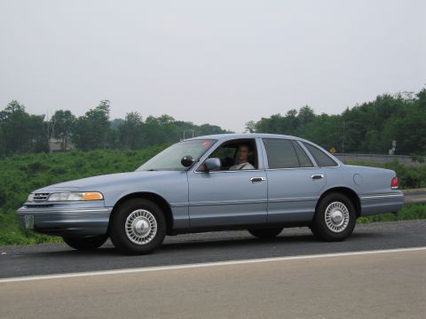 1991 Ford LTD Crown Victoria - A light blue 1991 Ford Crown Victoria LTD is parked on the shoulder of a road, with a driver visible inside.