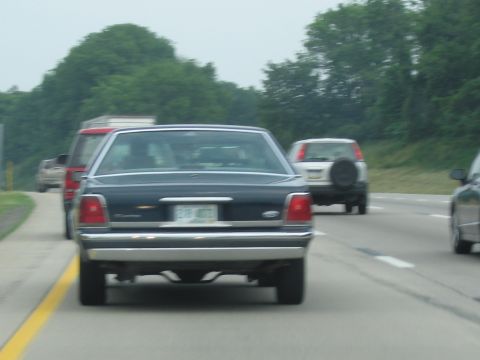 1991 Ford LTD Crown Victoria - A dark blue sedan drives on the highway behind other vehicles.