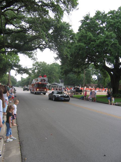 2000 Ford Crown Victoria - A parade passes by spectators on a tree-lined street, a fire truck and a sports car.