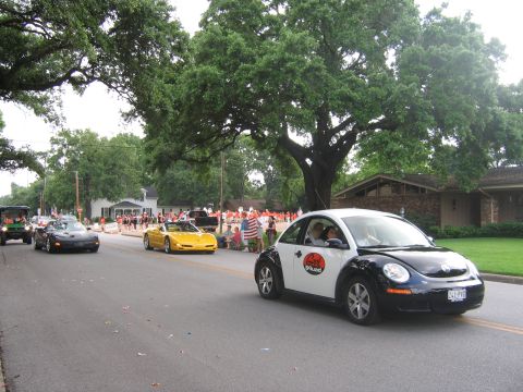 2000 Ford Crown Victoria - A two-tone Volkswagen Beetle participates in a parade, with other vehicles and spectators visible.