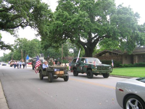 2000 Ford Crown Victoria - A military jeep and a camouflage truck participate in a parade, decorated with American flags.