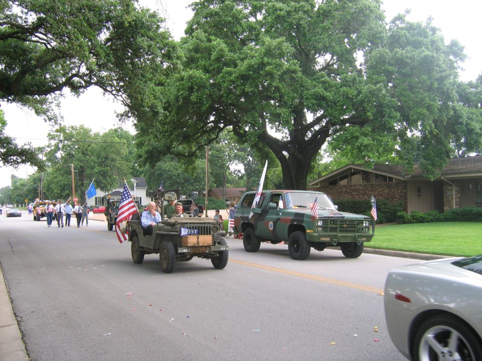 Green military jeep with American flag and camouflage truck in parade