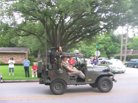 2000 Ford Crown Victoria - A man in camouflage drives a military-style jeep with a mounted machine gun during a parade.