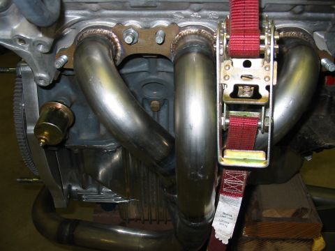 1993 Ford Taurus - Custom exhaust headers installed on an engine, secured with a red ratchet strap.