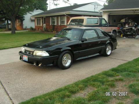 1988 Ford Mustang - 1988 Ford Mustang with custom hood and wheels, parked in front of a suburban house.