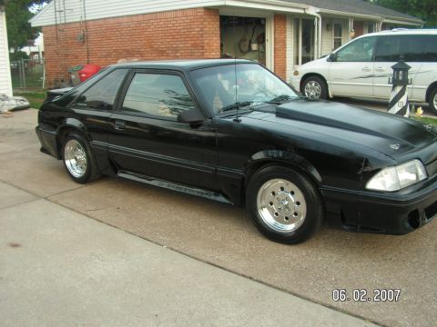 1988 Ford Mustang - A black coupe with aftermarket wheels and a cowl induction hood sits in a driveway.