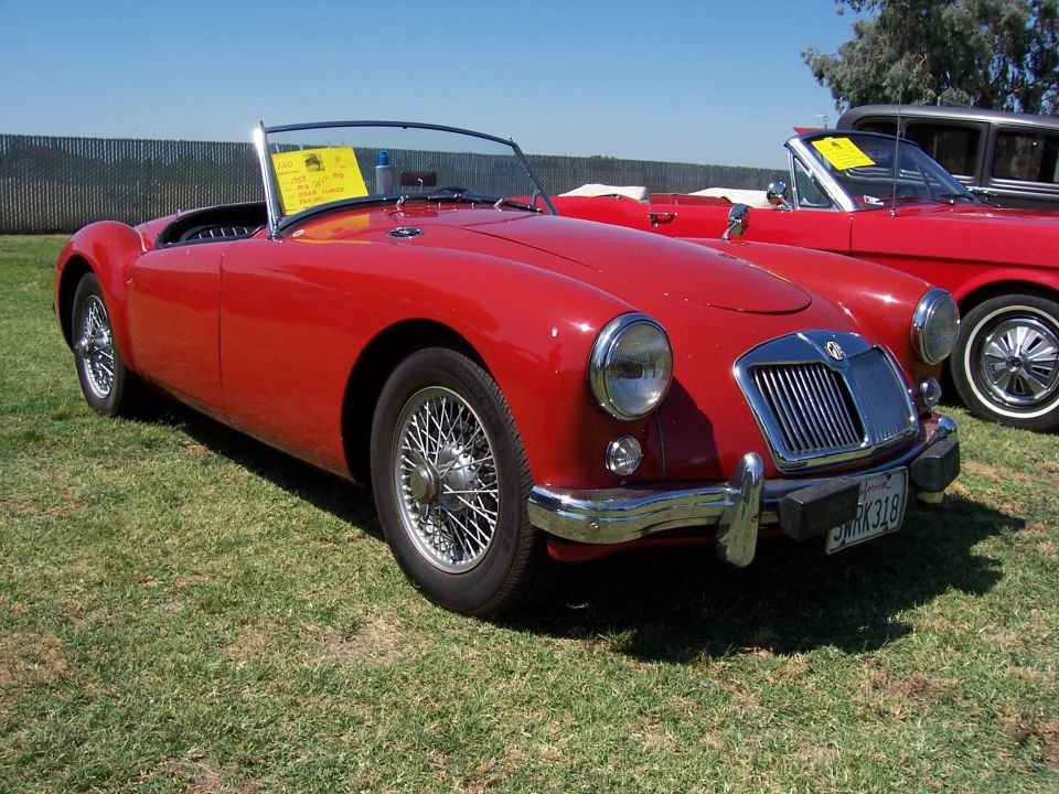 Red MGA convertible with wire wheels and a yellow sign on the dashboard