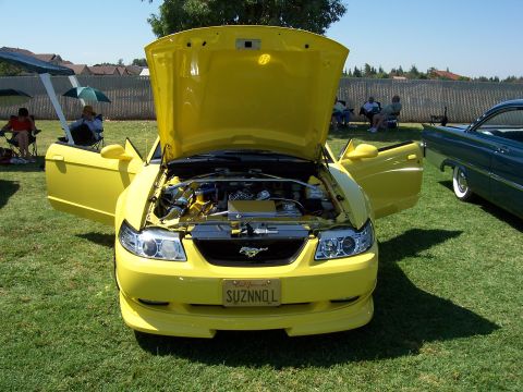 2002 Ford Mustang - A yellow 2002 Ford Mustang is displayed with its hood and doors open at an outdoor event.