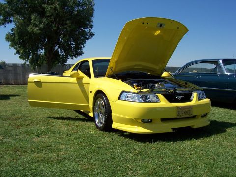 2002 Ford Mustang - A yellow Ford Mustang is displayed with its hood and driver's door open, revealing the engine compartment.