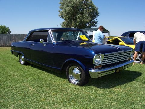 2002 Ford Mustang - A dark blue 1965 Nova coupe is parked on a grassy field with other vehicles in the background.