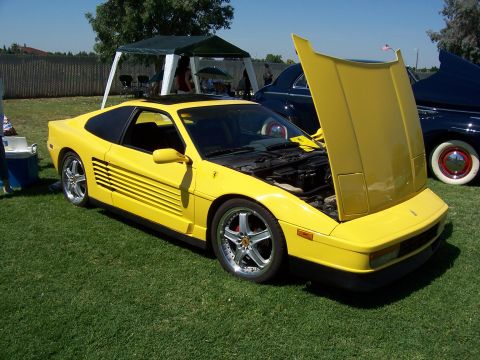 2002 Ford Mustang - A yellow Ferrari Testarossa is parked on grass with its hood open, next to another car.